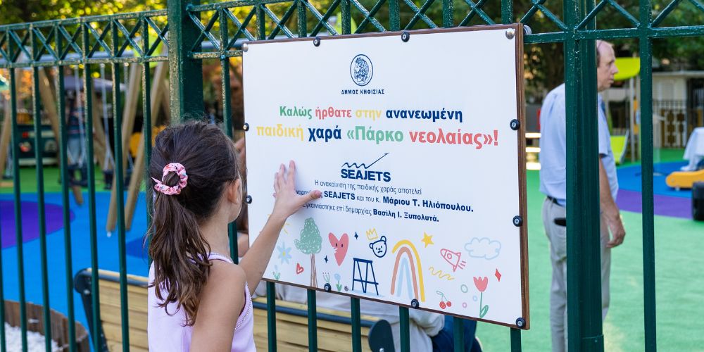 ένα κορίτσι που κοιτάει την ταμπέλα της παιδικής χαράς την οποία εγκαινίασε η SEAJETS
